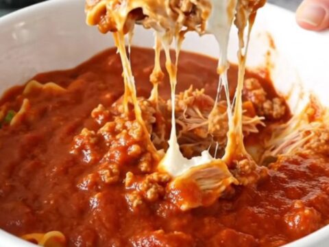 A black slow cooker filled with layers of ground turkey, ricotta, mozzarella, and marinara sauce.