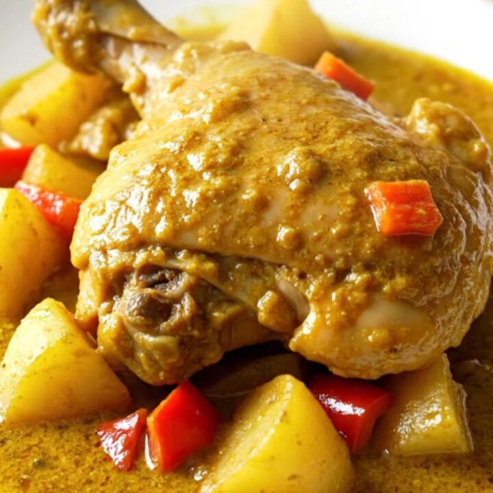 A close-up of a bowl filled with tender chicken thighs, chunks of potato, and red peppers in a thick, golden curry sauce.