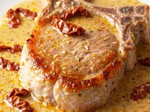 A close-up of tender, creamy pork chops in a slow cooker with sun-dried tomatoes and parmesan.