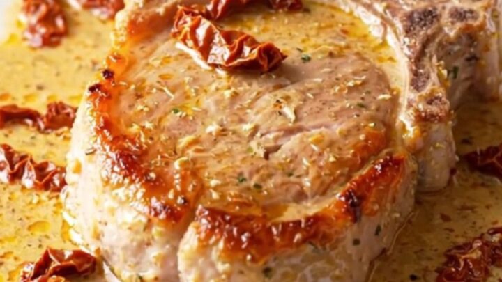 A close-up of tender, creamy pork chops in a slow cooker with sun-dried tomatoes and parmesan.