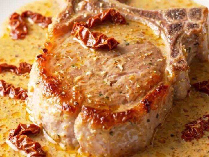 A close-up of tender, creamy pork chops in a slow cooker with sun-dried tomatoes and parmesan.