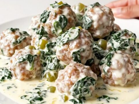 A slow cooker filled with creamy white queso meatballs, spinach, and green chiles on a speckled quartz countertop.
