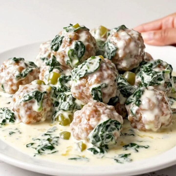 A slow cooker filled with creamy white queso meatballs, spinach, and green chiles on a speckled quartz countertop.