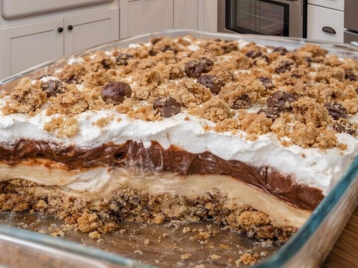 A slice of no-bake peanut butter pie with clear layers of cookie crust, peanut butter filling, chocolate ganache