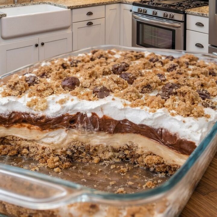 A slice of no-bake peanut butter pie with clear layers of cookie crust, peanut butter filling, chocolate ganache