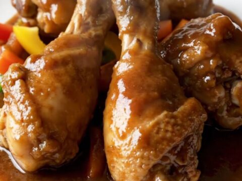 A close-up of tender Jamaican brown stew chicken with dark gravy in a slow cooker.