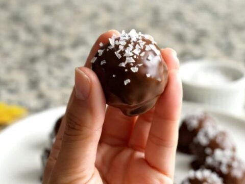 A plate of chocolate-dipped peanut butter buckeyes sprinkled with flaky salt.