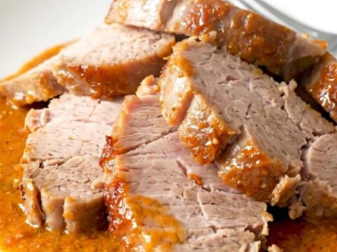 A top-down view of a crockpot filled with raw pork tenderloin, sun-dried tomatoes, and a creamy sauce.