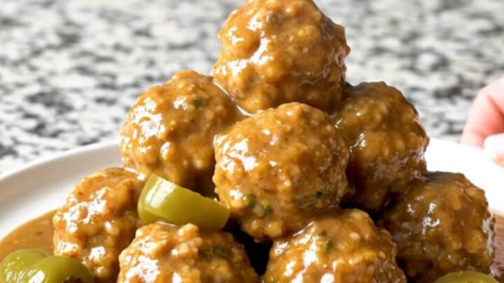 A close-up of tender turkey meatballs in a rich, buttery gravy with whole pepperoncini in a slow cooker.