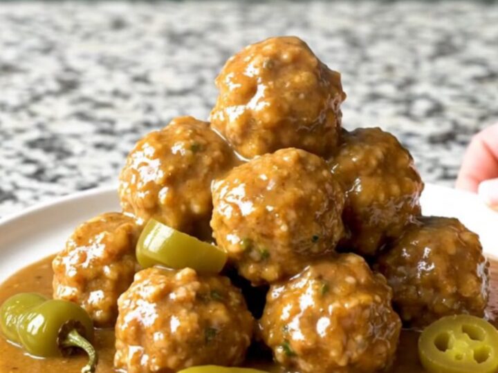 A close-up of tender turkey meatballs in a rich, buttery gravy with whole pepperoncini in a slow cooker.