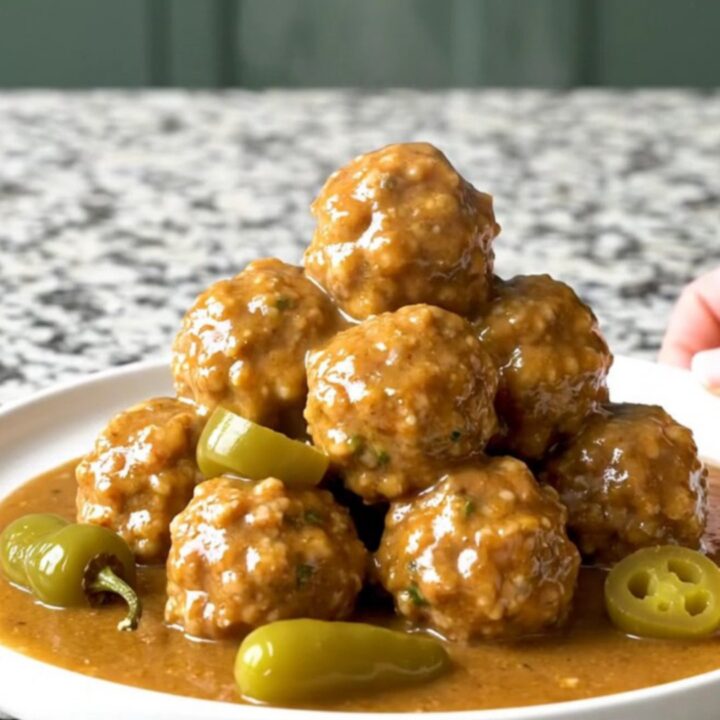 A close-up of tender turkey meatballs in a rich, buttery gravy with whole pepperoncini in a slow cooker.
