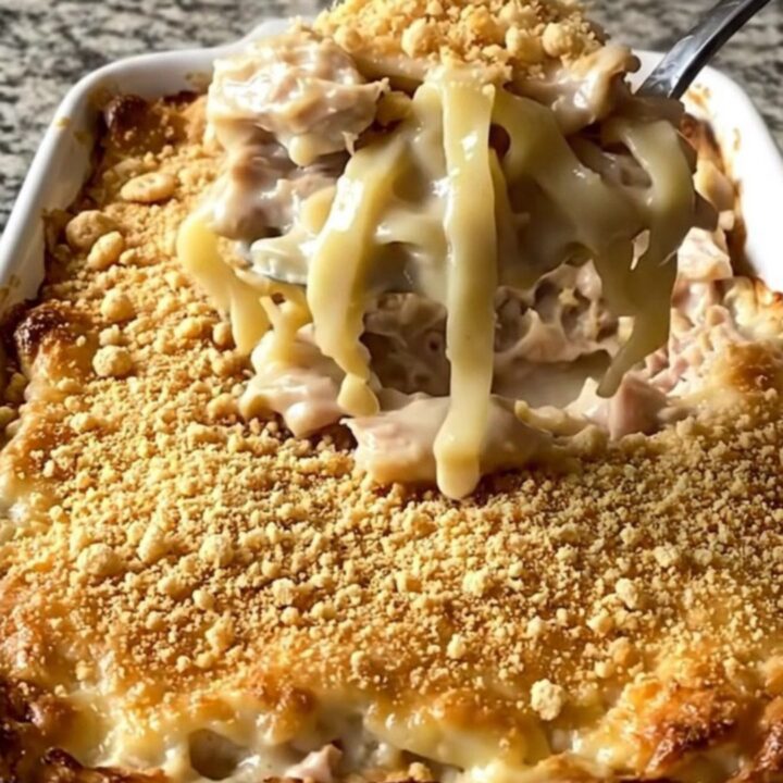 A top-down view of a golden, bubbly chicken and noodle bake in a white ceramic dish.