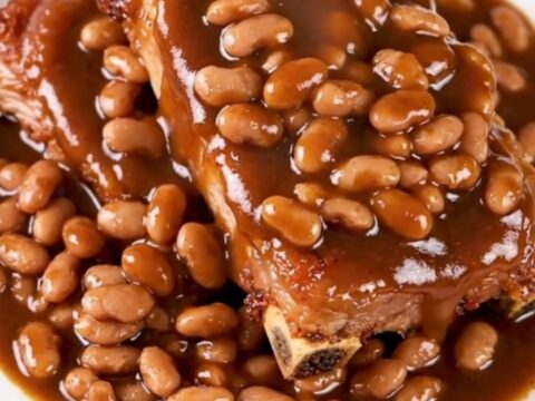 A close-up of tender, saucy country-style pork ribs served with baked beans on a white plate.
