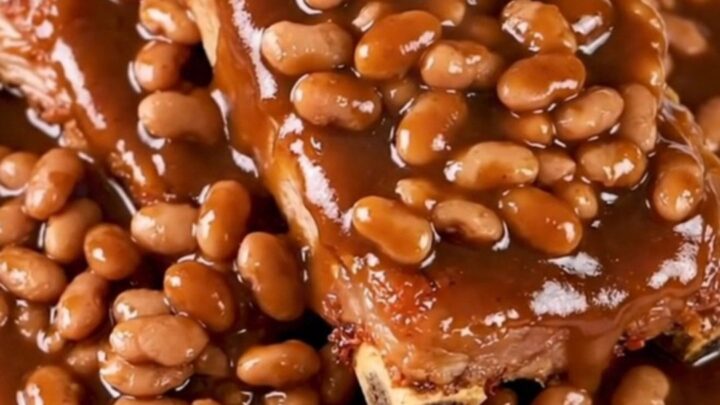 A close-up of tender, saucy country-style pork ribs served with baked beans on a white plate.