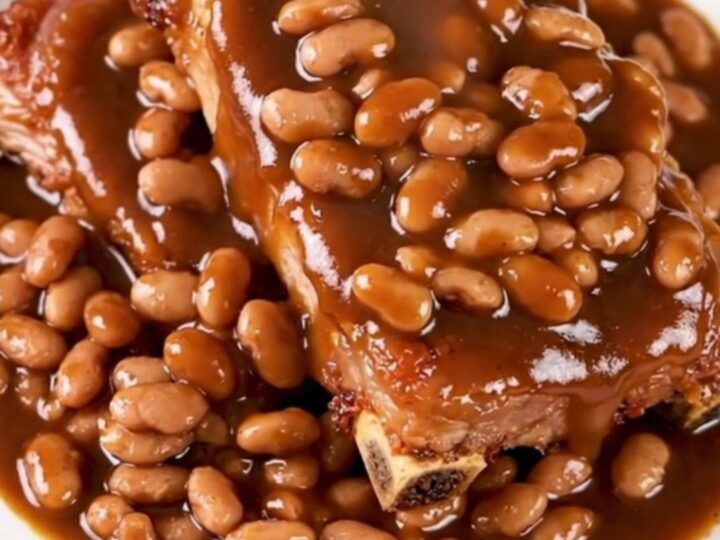 A close-up of tender, saucy country-style pork ribs served with baked beans on a white plate.