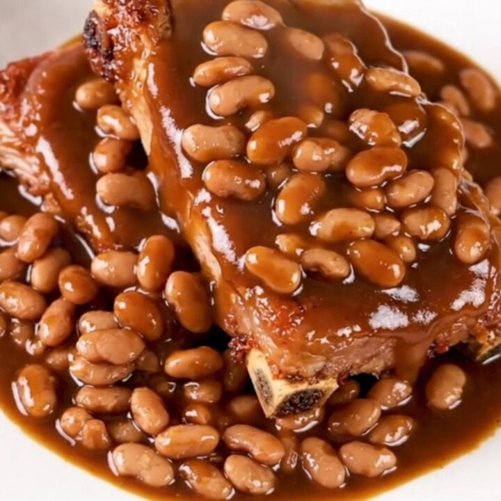 A close-up of tender, saucy country-style pork ribs served with baked beans on a white plate.