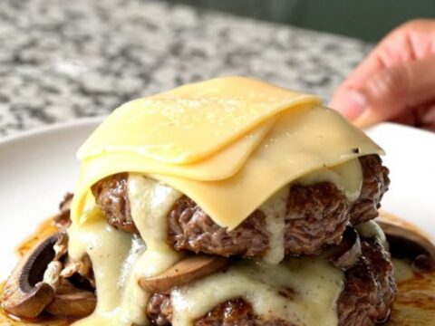 Slow cooker mushroom Swiss burger steaks with melted cheese on a white plate.