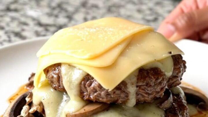 Slow cooker mushroom Swiss burger steaks with melted cheese on a white plate.