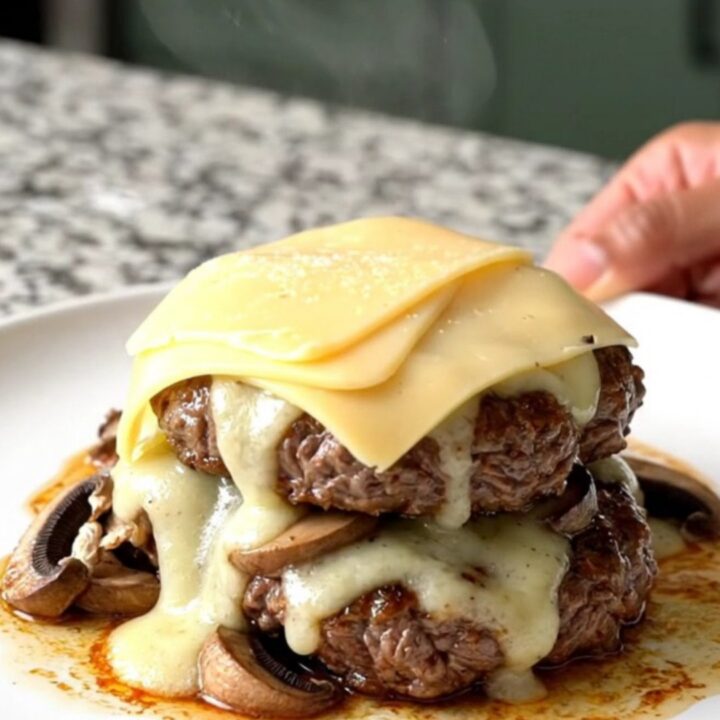 Slow cooker mushroom Swiss burger steaks with melted cheese on a white plate.