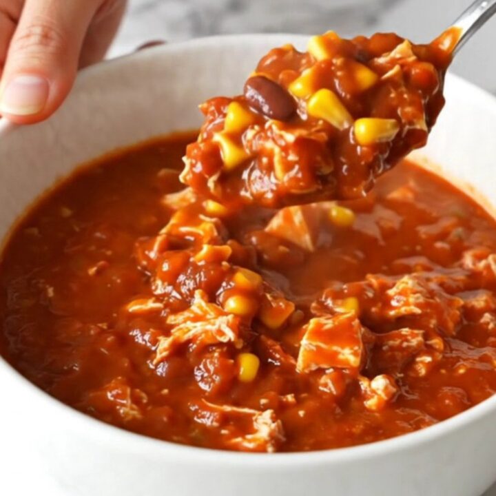 A top-down view of a black slow cooker filled with raw ground turkey, beans, corn, and red enchilada sauce.