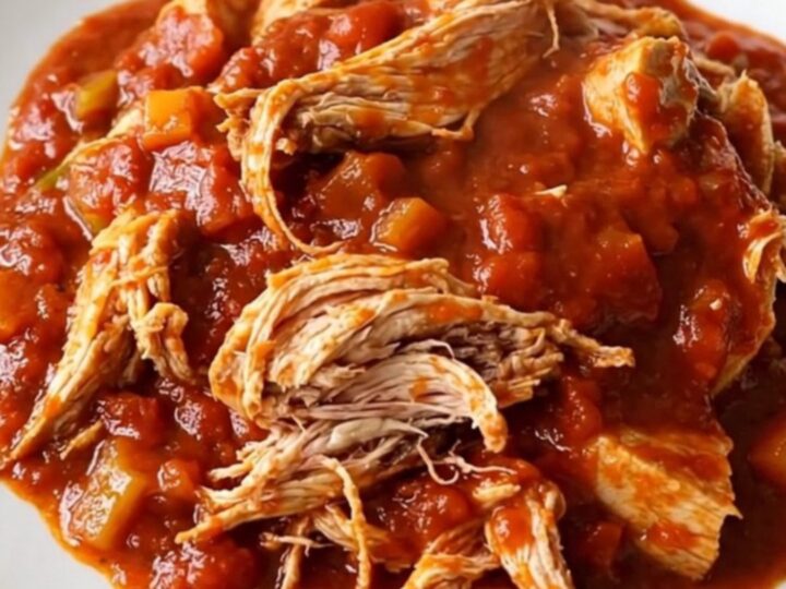 A stainless steel slow cooker filled with chicken ragu, showing tender chicken pieces and vibrant vegetables in a rich tomato