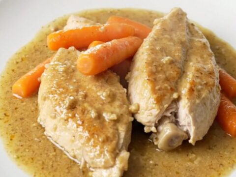 A top-down view of raw chicken breasts and baby carrots seasoned in a black oval slow cooker.
