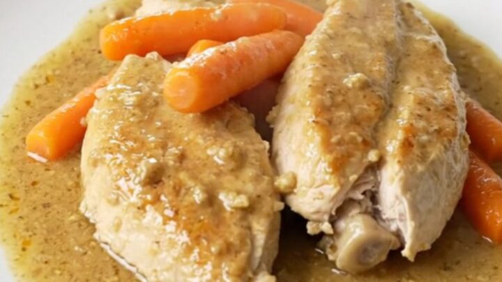 A top-down view of raw chicken breasts and baby carrots seasoned in a black oval slow cooker.