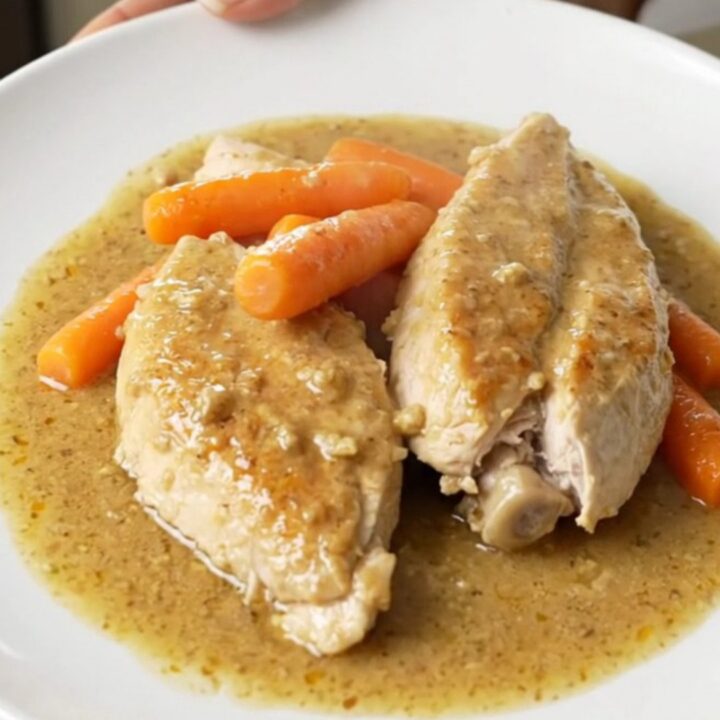 A top-down view of raw chicken breasts and baby carrots seasoned in a black oval slow cooker.