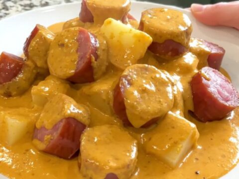 A top-down view of a slow cooker filled with kielbasa, potatoes, and a creamy cheese sauce, ready to be served.