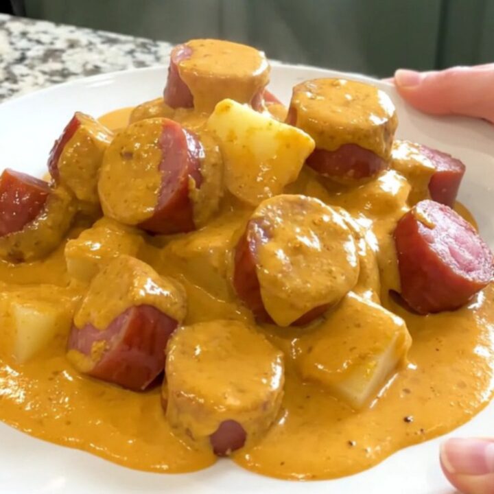 A top-down view of a slow cooker filled with kielbasa, potatoes, and a creamy cheese sauce, ready to be served.