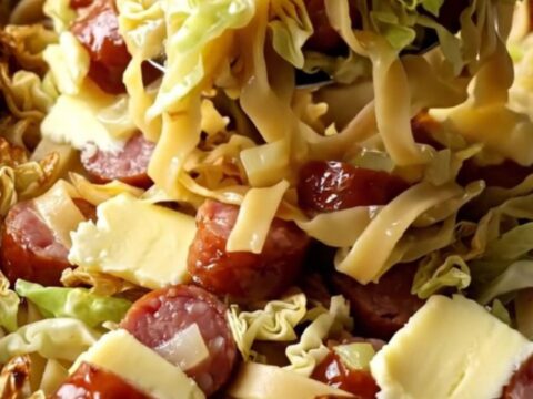 A large rectangular baking dish filled with golden baked egg noodles, tender cabbage, and sliced smoked kielbasa.