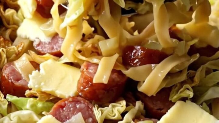 A large rectangular baking dish filled with golden baked egg noodles, tender cabbage, and sliced smoked kielbasa.