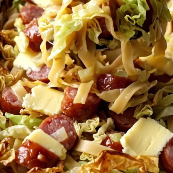 A large rectangular baking dish filled with golden baked egg noodles, tender cabbage, and sliced smoked kielbasa.