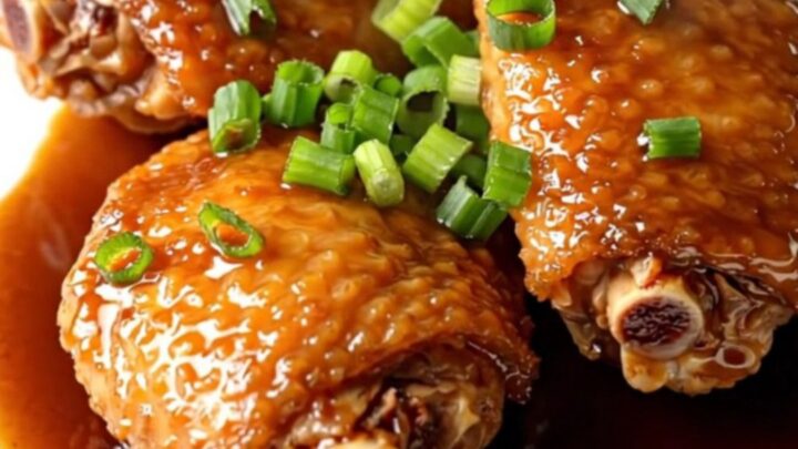 A high-angle shot of tender, braised chicken thighs in a slow cooker with a rich, dark shoyu glaze.