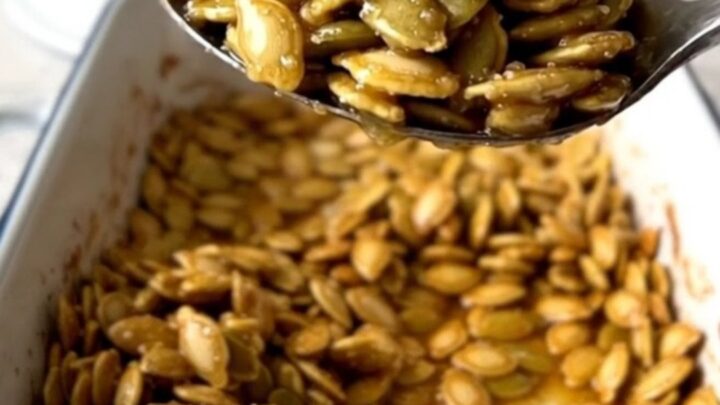 A large rectangular baker filled with golden, cinnamon-dusted roasted pumpkin seeds on a speckled quartz countertop.