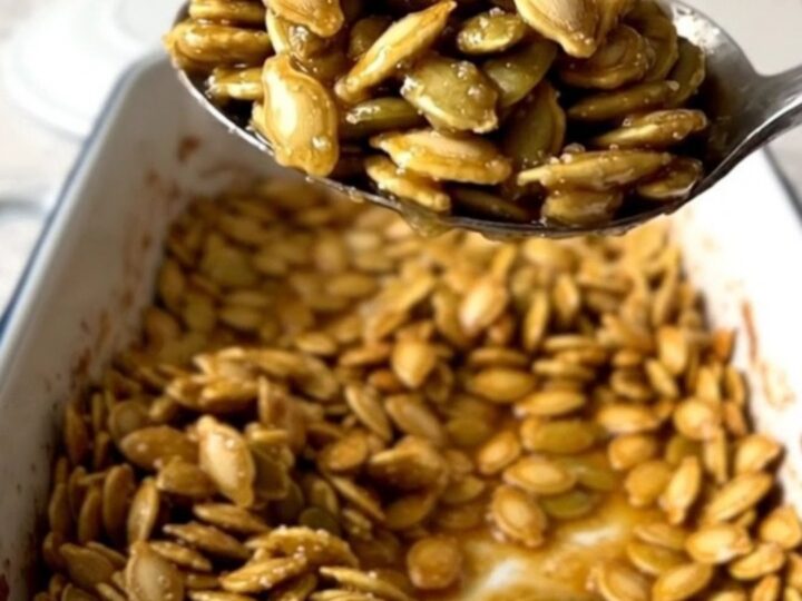 A large rectangular baker filled with golden, cinnamon-dusted roasted pumpkin seeds on a speckled quartz countertop.