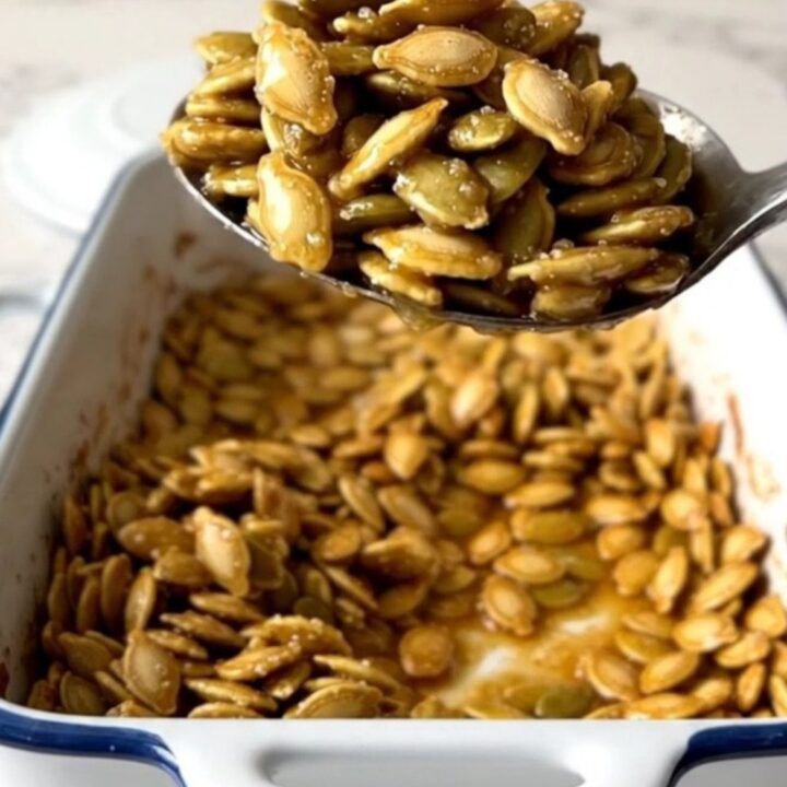 A large rectangular baker filled with golden, cinnamon-dusted roasted pumpkin seeds on a speckled quartz countertop.