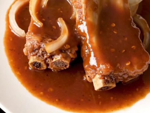 A close-up of tender, glazed pork spareribs arranged in a white slow cooker with onions and a sticky red sauce.