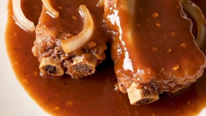 A close-up of tender, glazed pork spareribs arranged in a white slow cooker with onions and a sticky red sauce.