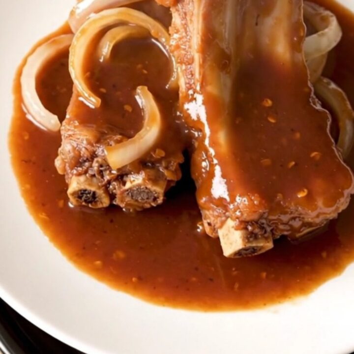 A close-up of tender, glazed pork spareribs arranged in a white slow cooker with onions and a sticky red sauce.