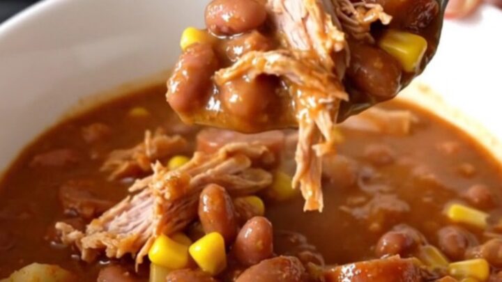 A top-down view of a black slow cooker filled with raw ground turkey, sliced smoked sausage, cubed potatoes, and beans.