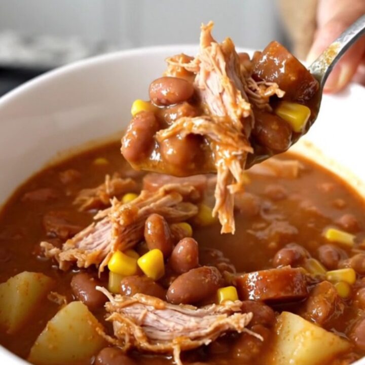 A top-down view of a black slow cooker filled with raw ground turkey, sliced smoked sausage, cubed potatoes, and beans.