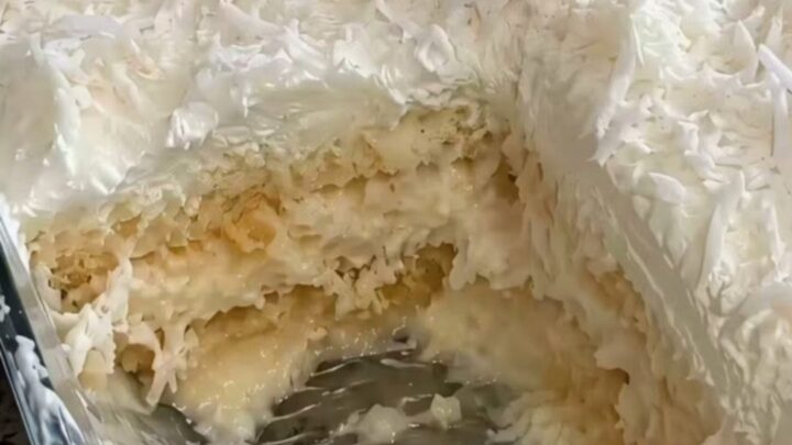 A decadent, creamy slice of no-bake coconut cake being lifted from a glass dish.