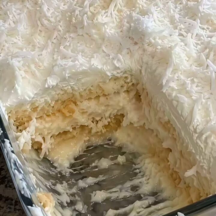 A decadent, creamy slice of no-bake coconut cake being lifted from a glass dish.