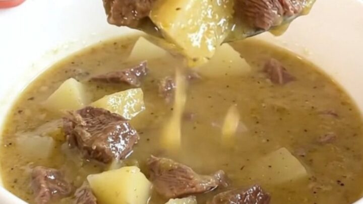 A rustic white bowl filled with creamy steak and potato soup, garnished with fresh herbs and steam rising from the surface.