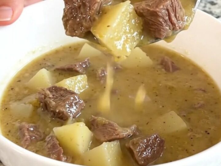 A rustic white bowl filled with creamy steak and potato soup, garnished with fresh herbs and steam rising from the surface.