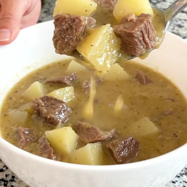 A rustic white bowl filled with creamy steak and potato soup, garnished with fresh herbs and steam rising from the surface.