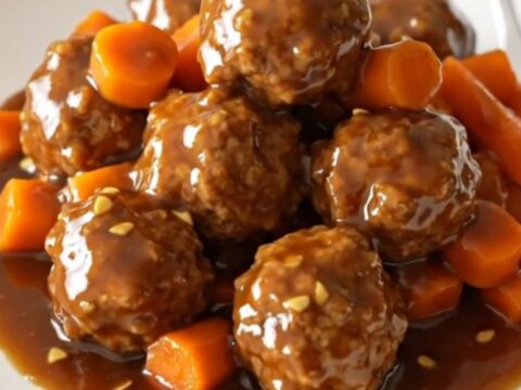 A close-up view of Mongolian beef meatballs glazed in a dark, glossy sauce with shredded carrots in a slow cooker.