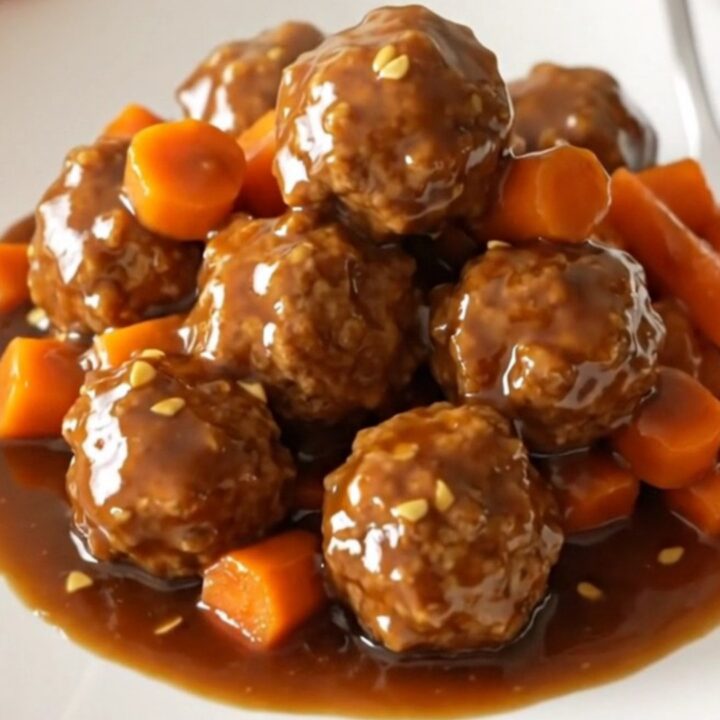 A close-up view of Mongolian beef meatballs glazed in a dark, glossy sauce with shredded carrots in a slow cooker.