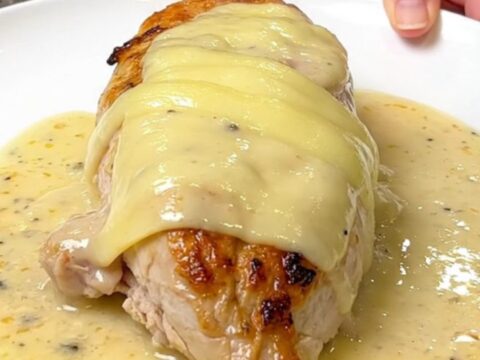 A close-up of tender chicken breasts topped with melted Swiss cheese in a creamy sauce.